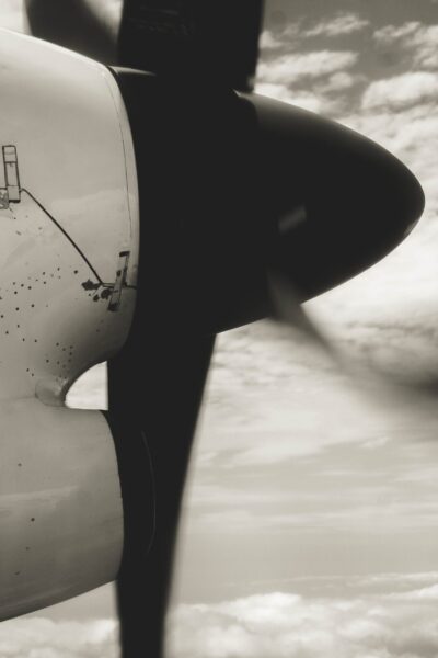 Black and white, close-up view of an airplane propeller in flight, spinning against a cloudy sky backdrop.