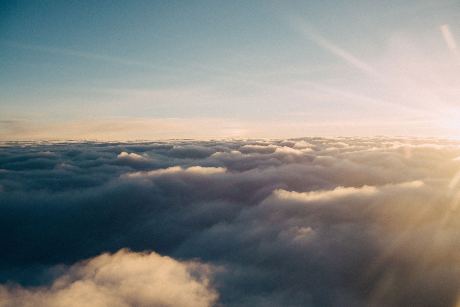 Golden sunlight peeks over a vast sea of clouds, casting a warm glow