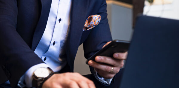 Image of a man with a light shirt and dark suit holding up his phone