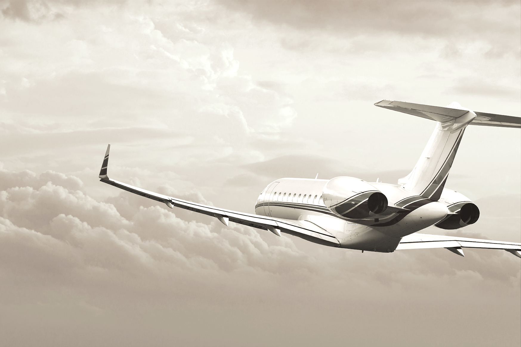 Image of a private jet flying above the clouds at sunset. Grey scale