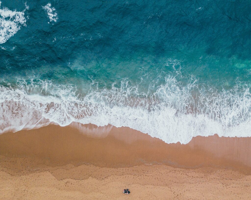 Bird eyes view of a couple sitting at a beach with light waves crashing over