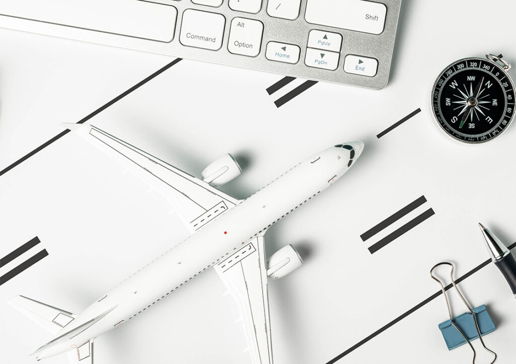 Image of a white model aircraft on a drawn runway, black compass, blue clip and a pen next to a keyboard