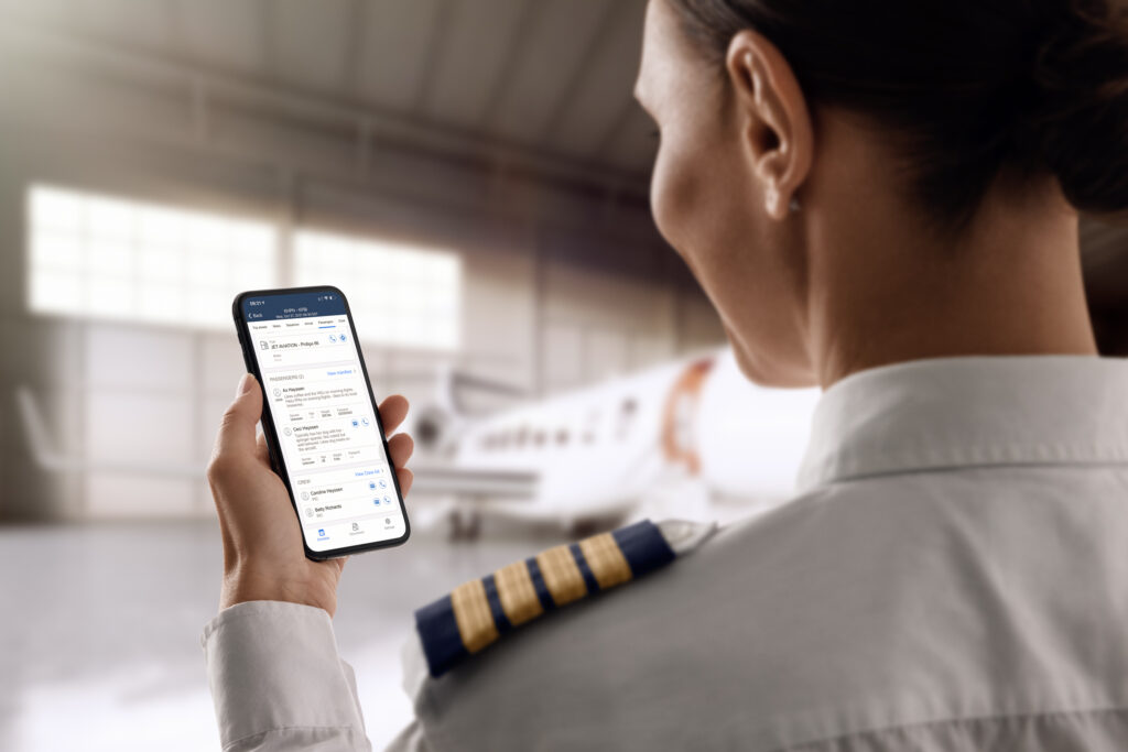 Image of a pilot taken from behind holding up her phone with the fuel app, a jet is in the blurry background