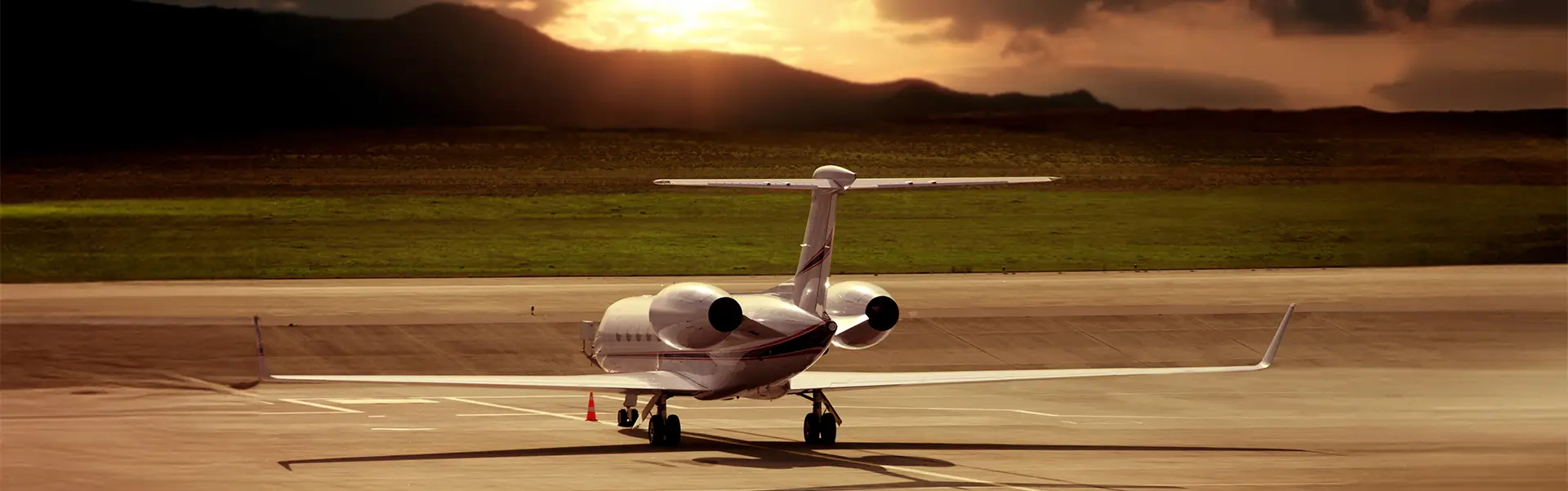 A private jet sitting on the tarmac with mountains and sunlit clouds in the background.