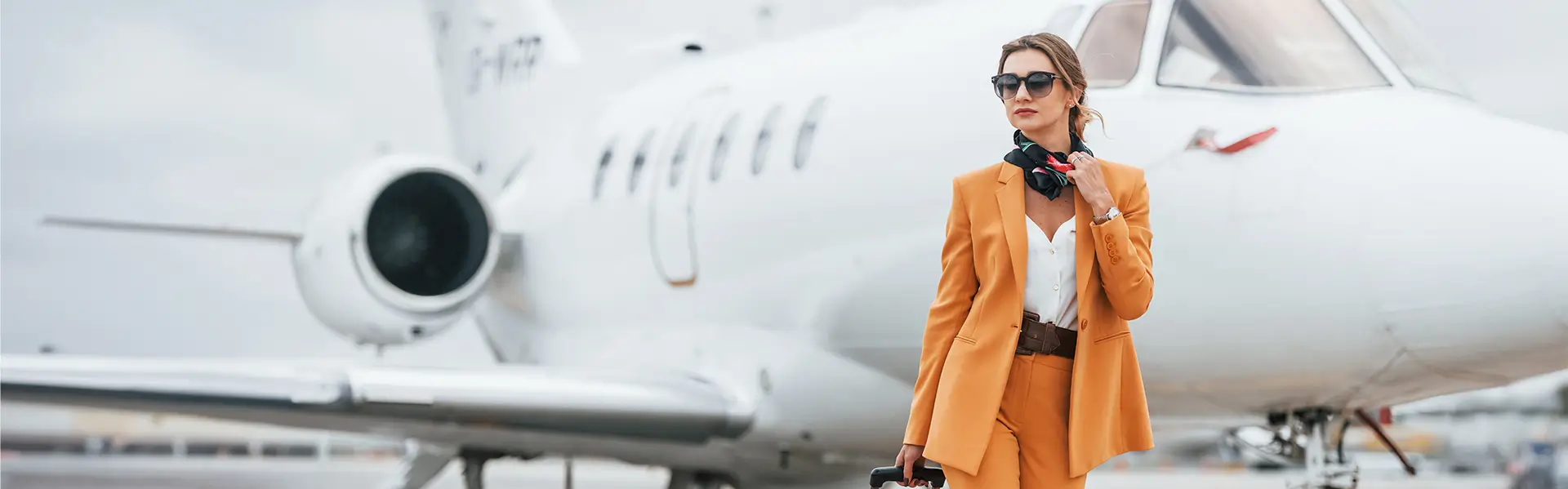 A private jet sitting on the tarmac with a female passenger in the foreground.