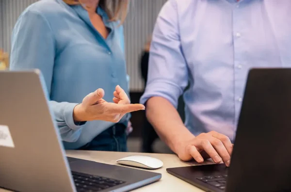 Two people collaborating on a laptop, one pointing at the screen, both wearing blue shirts