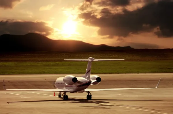 A private jet sitting on the tarmac with mountains and sunlit clouds in the background.