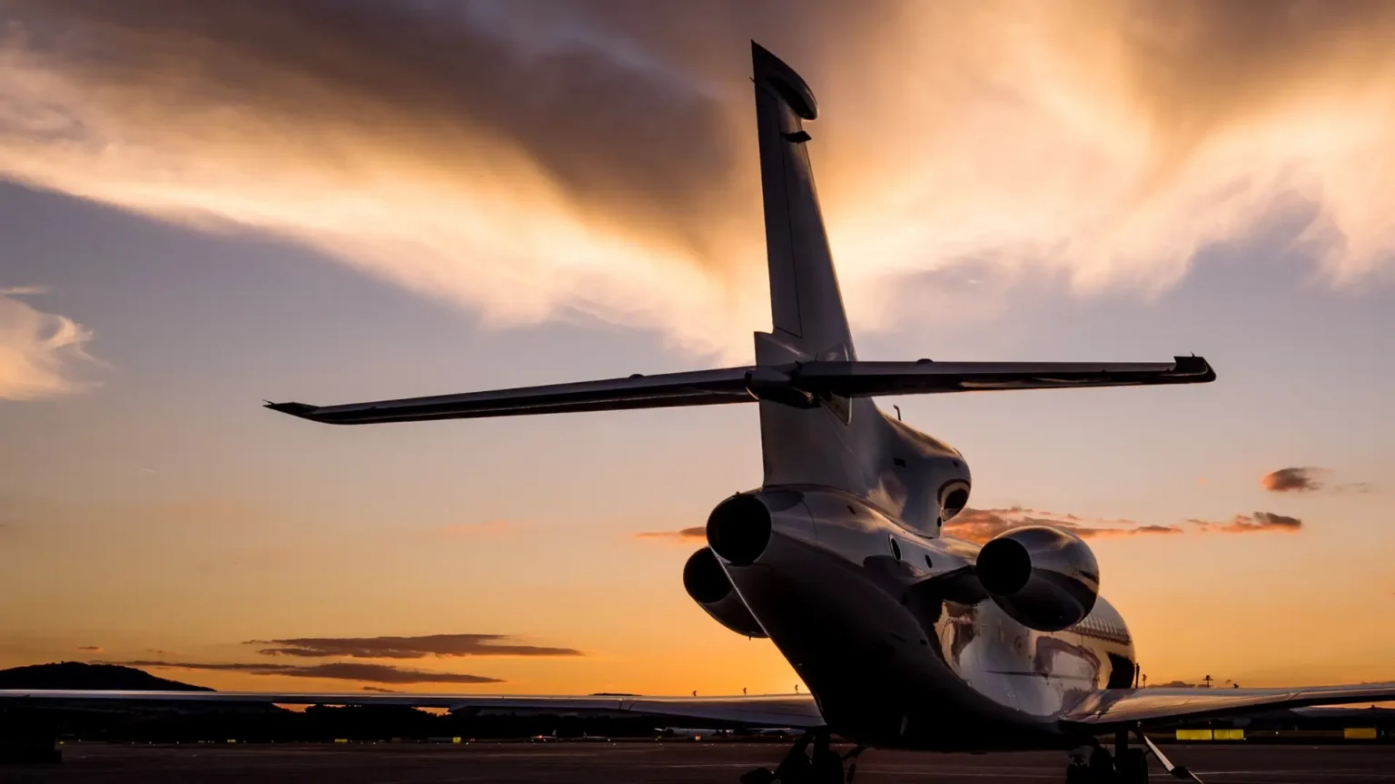 Private jet sitting on tarmac at sunset, rear view.
