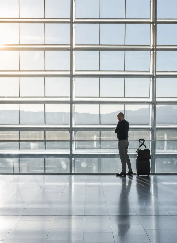 A man is talking on the phone at an airport in front of a big window, looking out at the runway.